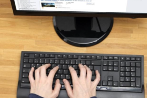 schwarze Tastatur vor PC beidhändig bedient